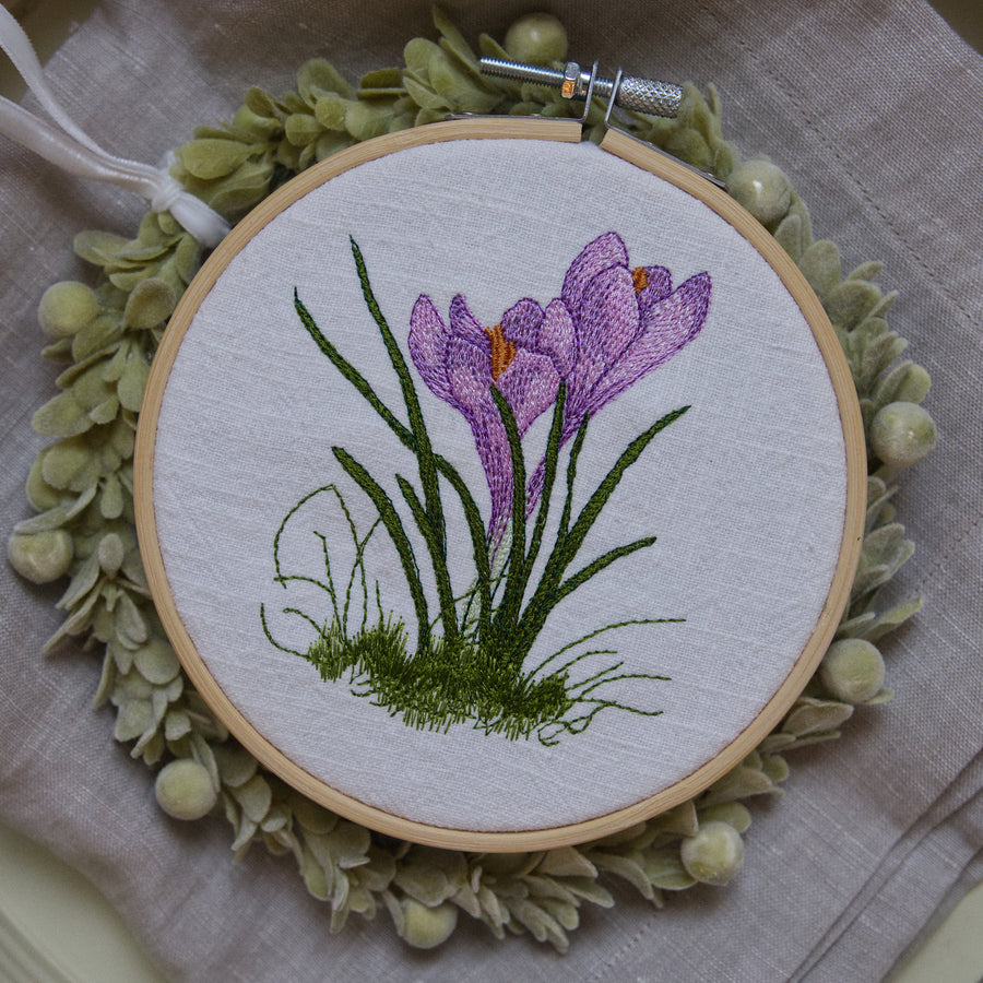 Stickdatei Krokus, zartes Frühlingsmotiv mit violetter Blüte und feinem Gras, detailreiche Maschinenstickerei auf heller Leinenware im Stickrahmen