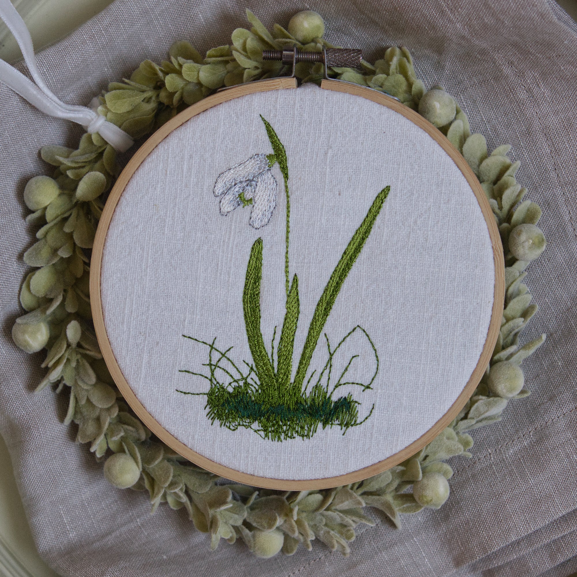 Stickdatei Schneeglöckchen, zartes Frühlingsmotiv mit feiner Blüte und Gräsern, gestickt auf heller Leinenware im Stickrahmen